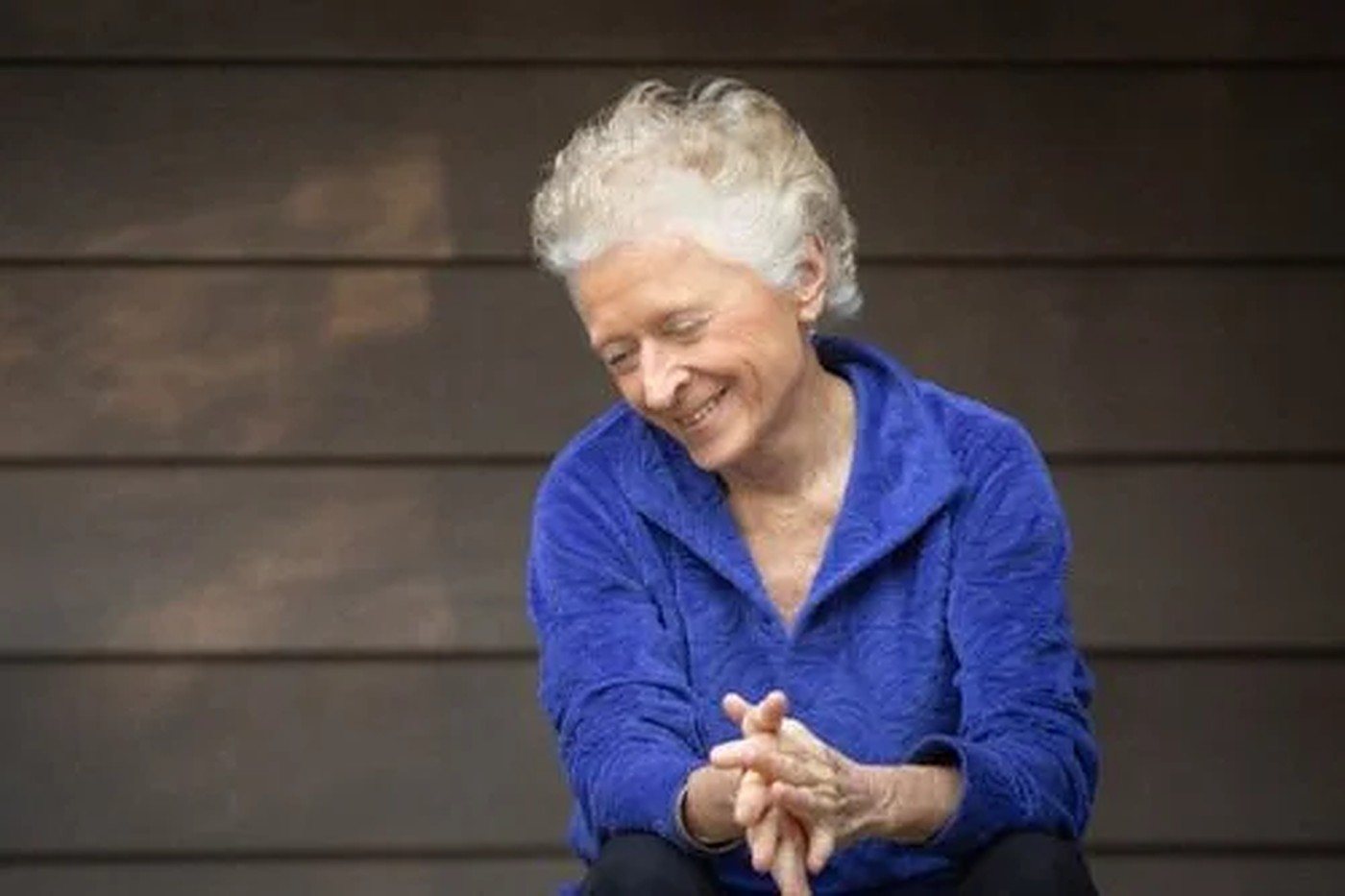 Marti Spiegelman, smiling, seated against a timber wall